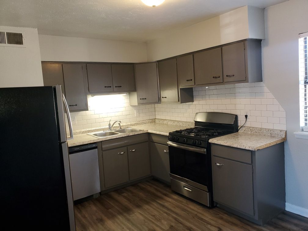 A kitchen with gray cabinets , a black refrigerator , a stove , and a sink.