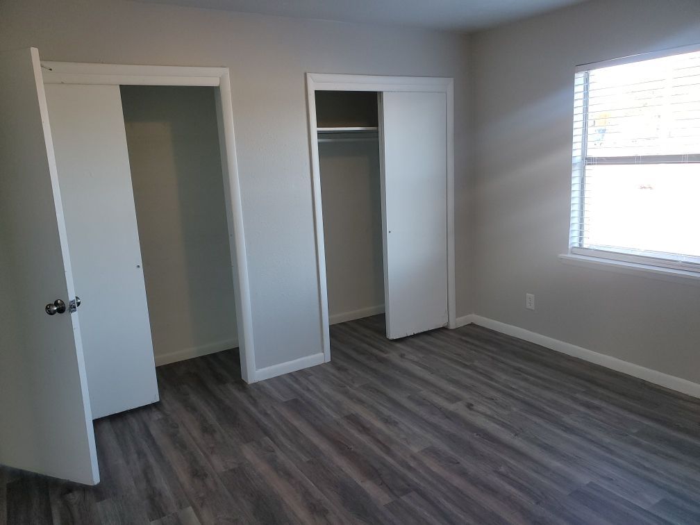 A bedroom with hardwood floors , two closets and a window.