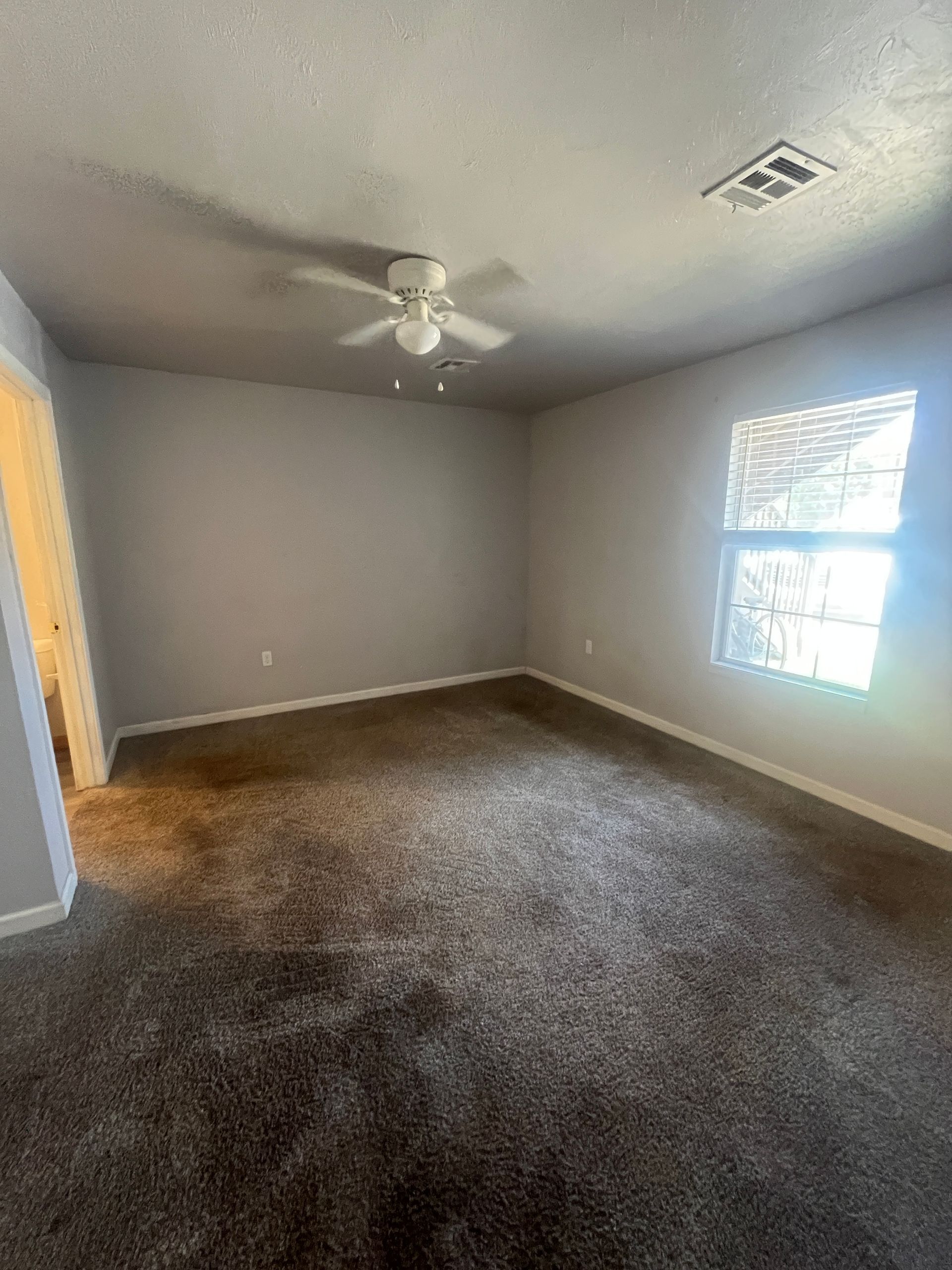 An empty bedroom with a ceiling fan and a window.