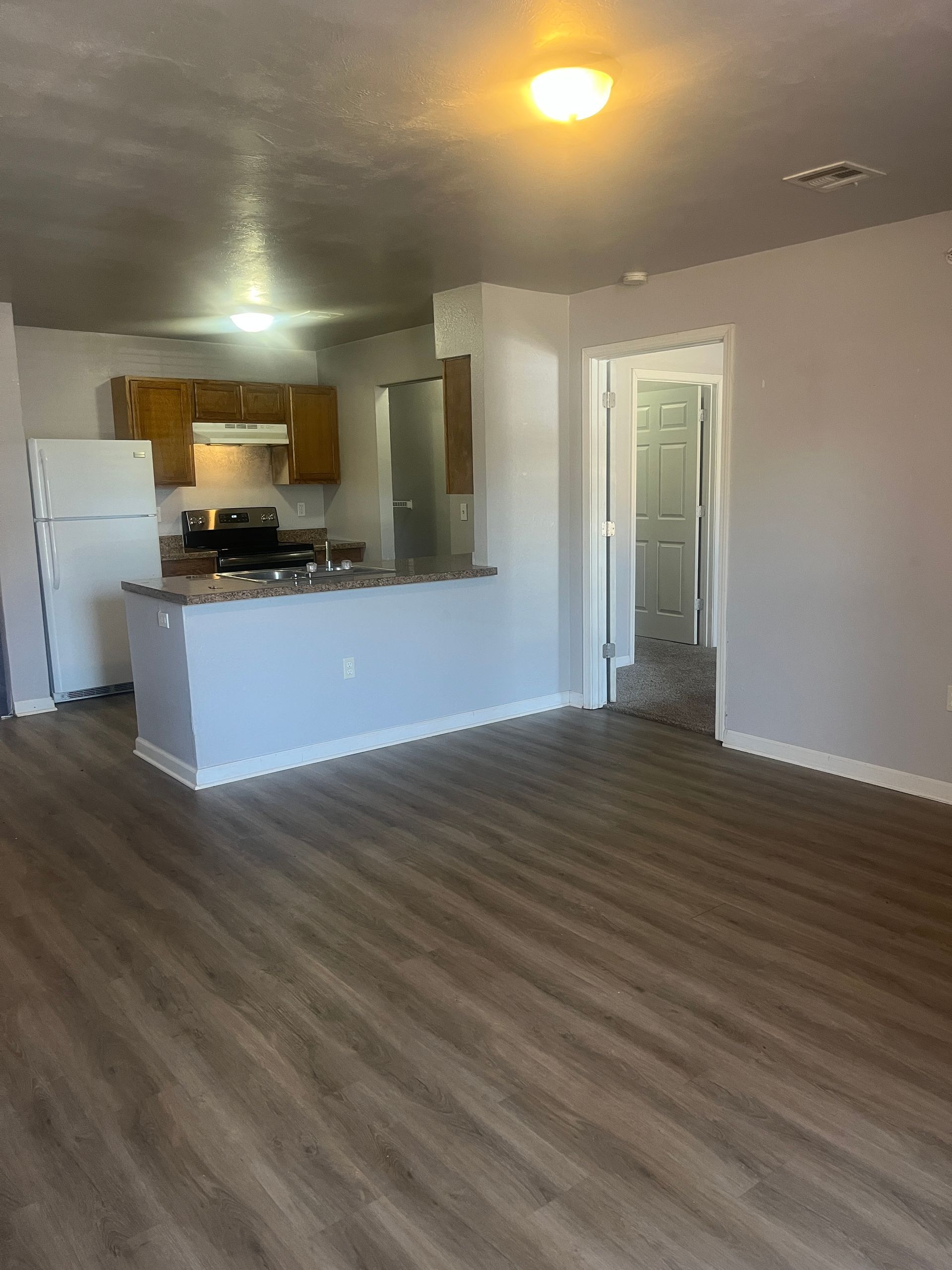 A living room with hardwood floors and a kitchen in the background.