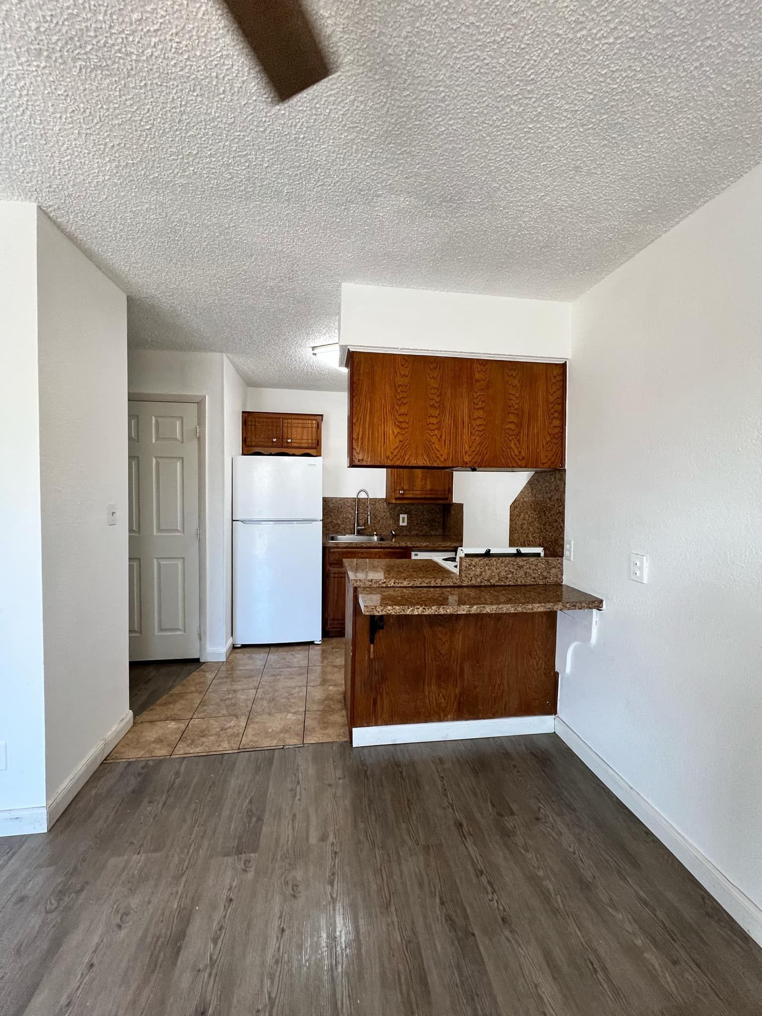 A kitchen with wooden cabinets , a refrigerator , and a ceiling fan.