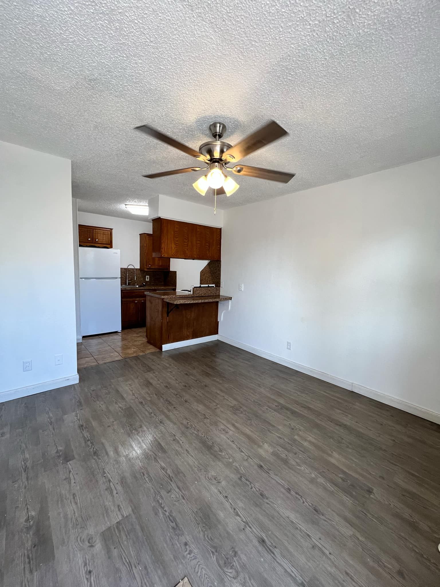 A living room with a ceiling fan and a kitchen in the background.