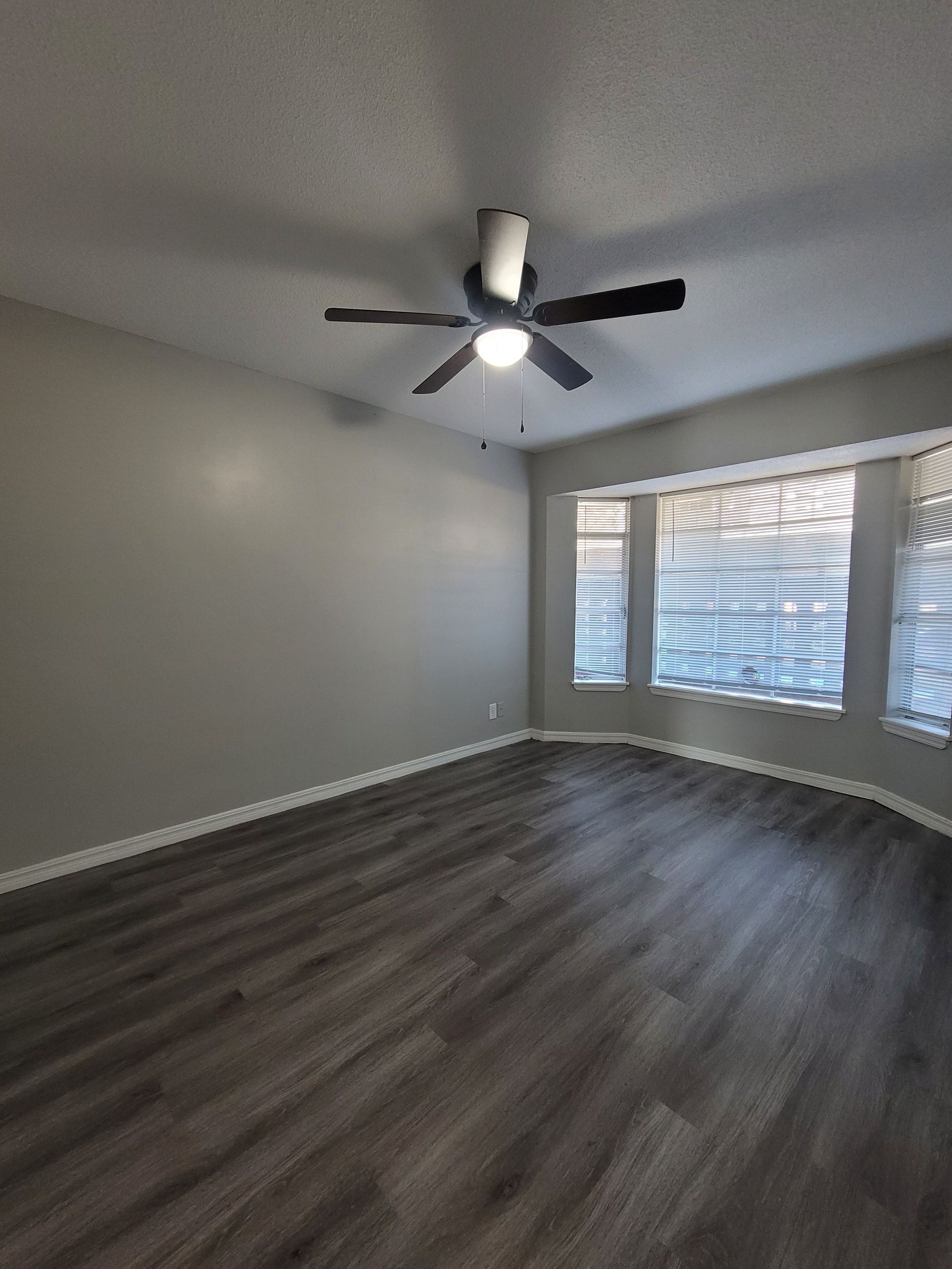 An empty living room with hardwood floors and a ceiling fan.