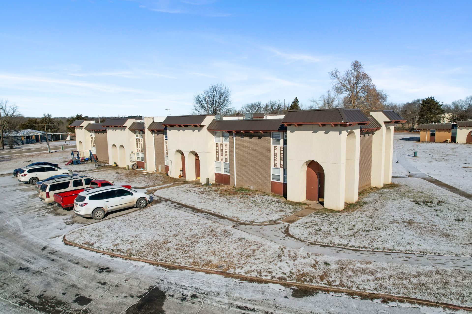 A row of cars are parked in front of a building in the snow.