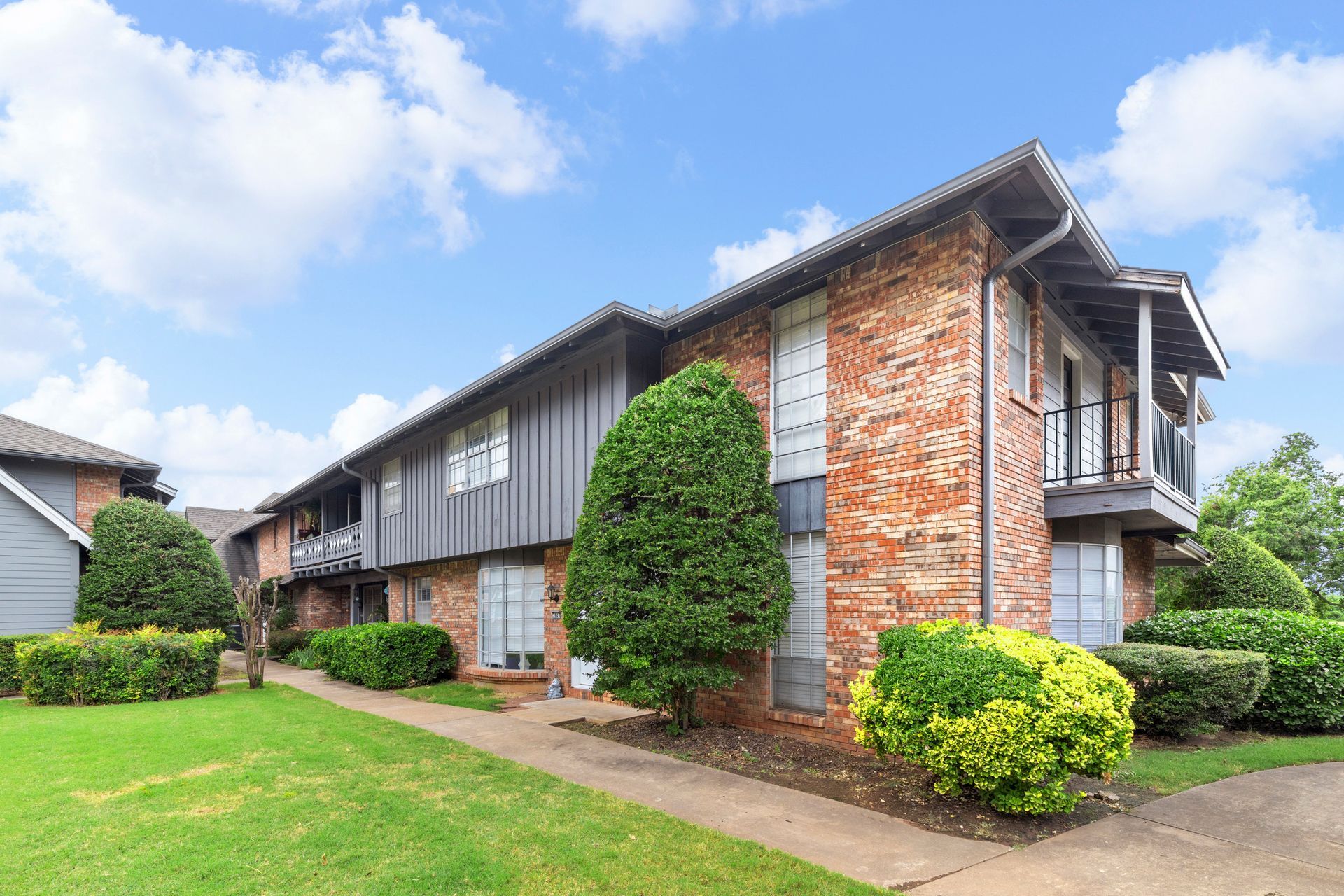 Apartment building with brick exterior and green lawn under a partly cloudy sky.