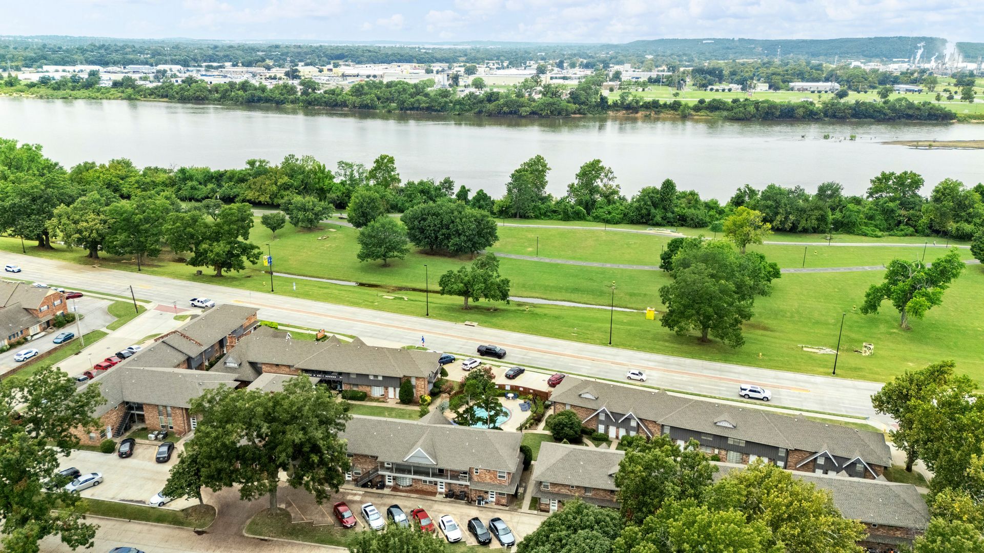 Aerial view of apartments, green park, and a wide river under a cloudy sky.