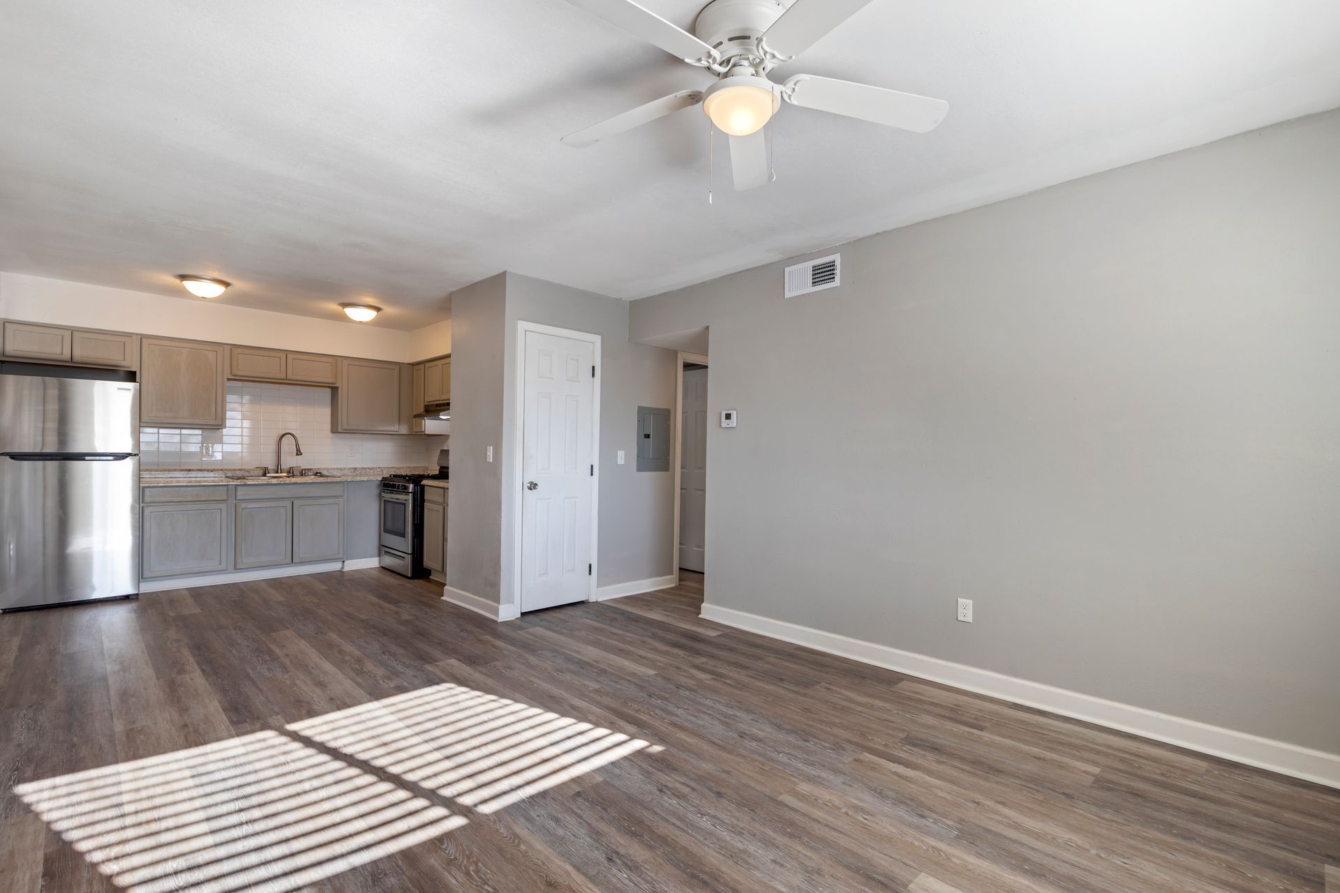 A living room with a ceiling fan and a kitchen in the background.