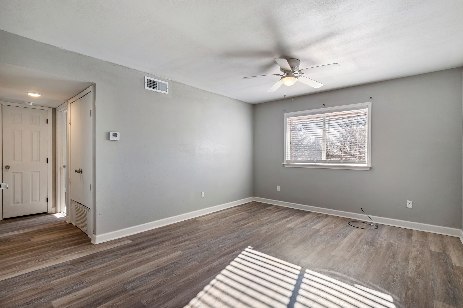 An empty living room with a ceiling fan and a window.