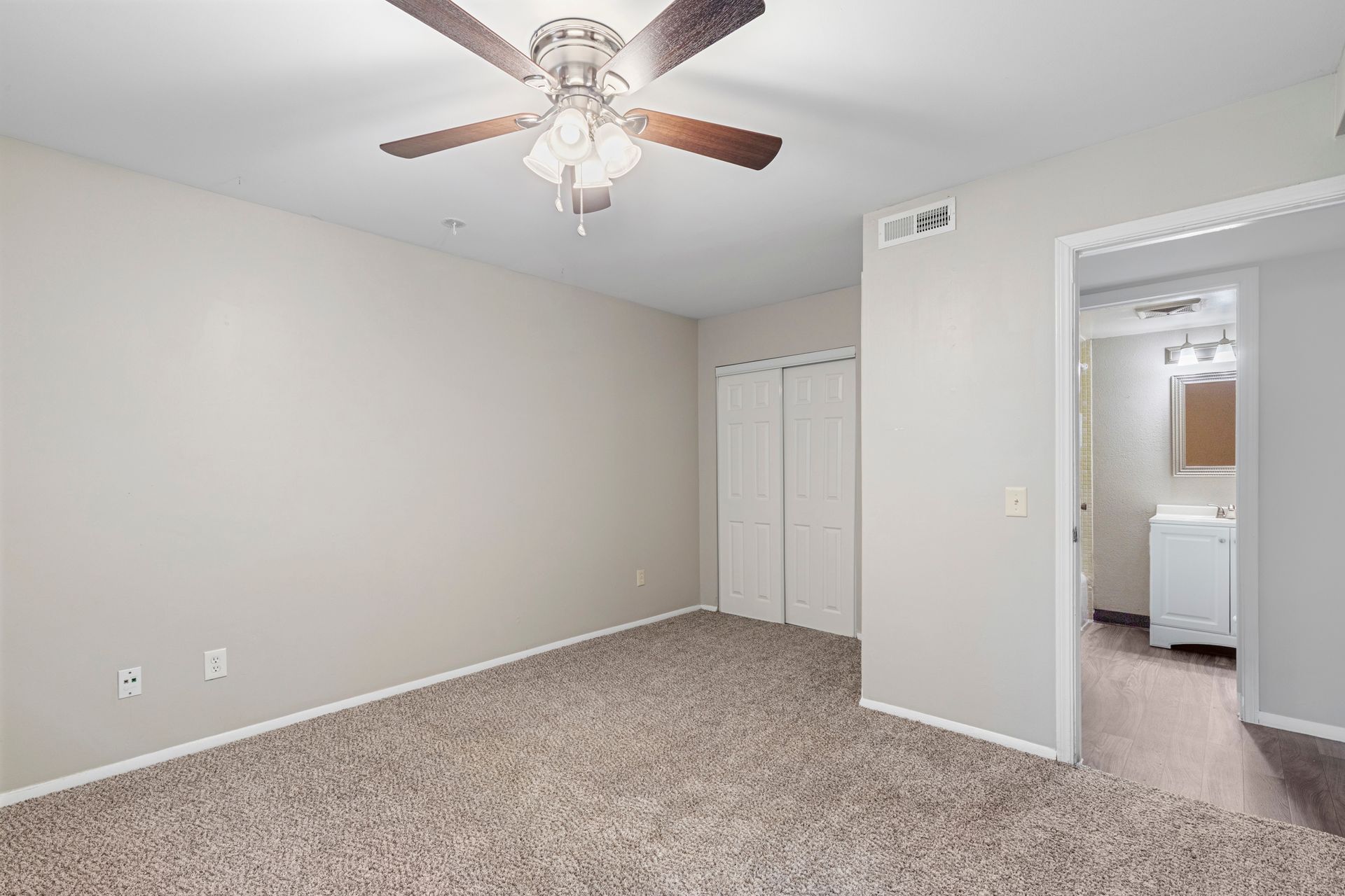 Bedroom with carpet, closet, and doorway to bathroom. Ceiling fan with lights.