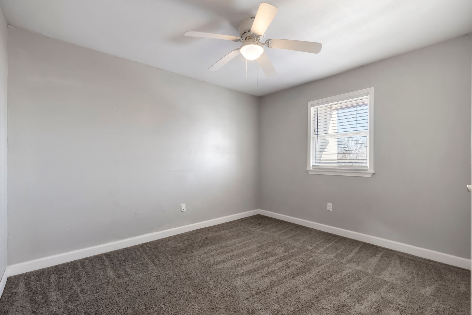 An empty bedroom with a ceiling fan and a window.