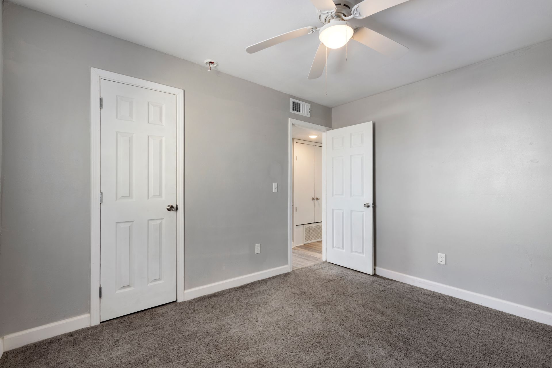 An empty bedroom with a ceiling fan and two doors.