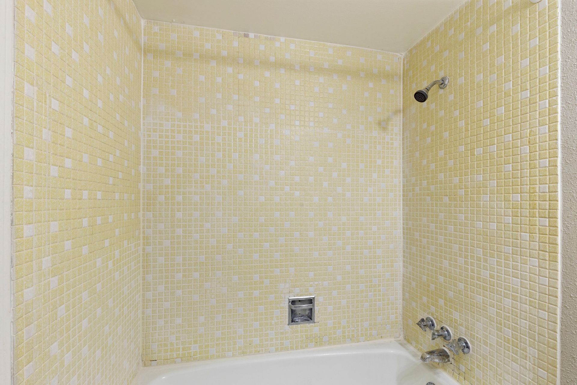 Yellow tiled shower stall with white tub and fixtures.