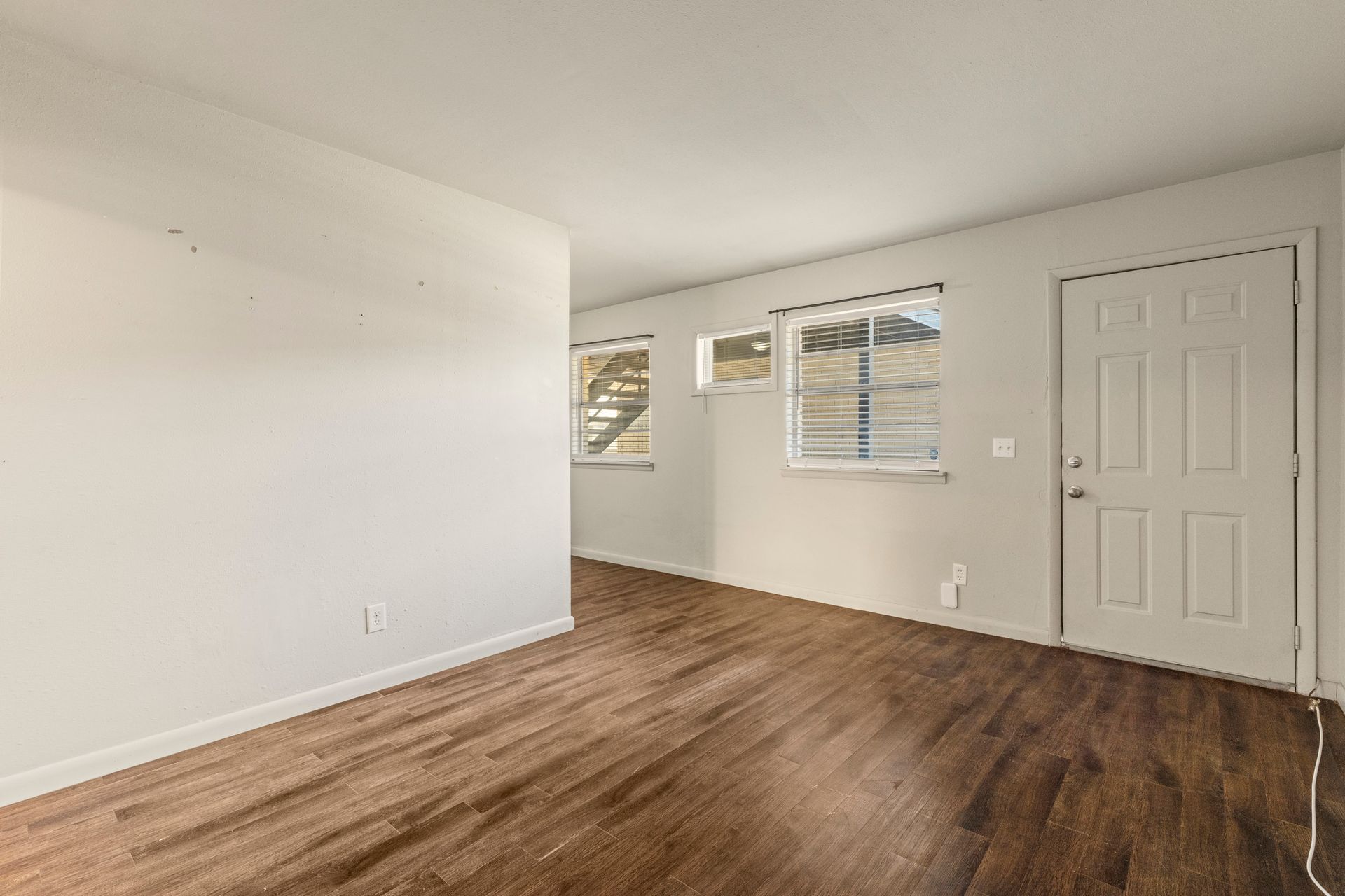 An empty living room with hardwood floors and white walls.