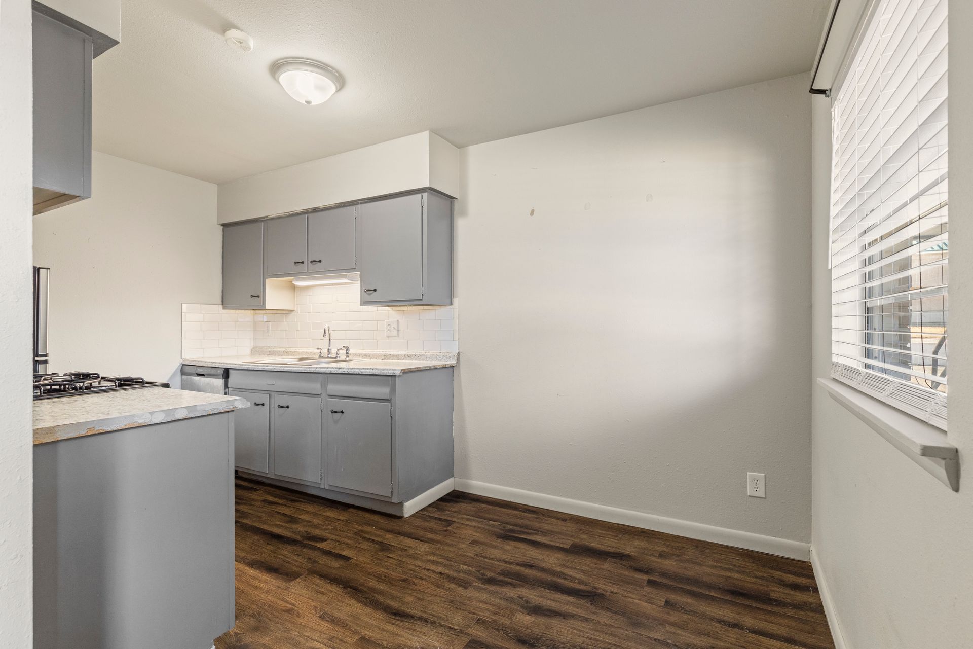 A kitchen with gray cabinets and wooden floors and a window.
