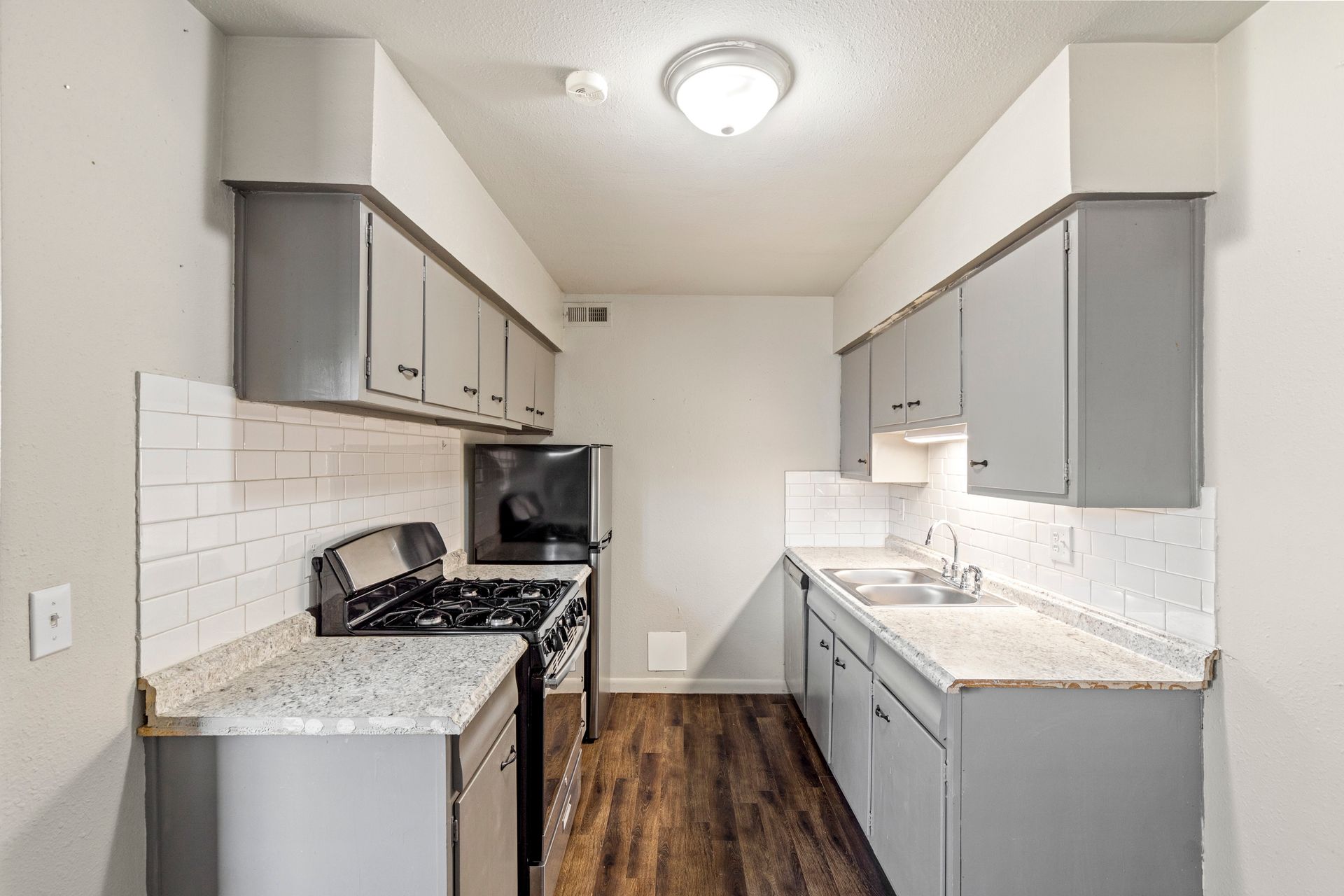 A kitchen with gray cabinets , a stove , a sink , and a microwave.