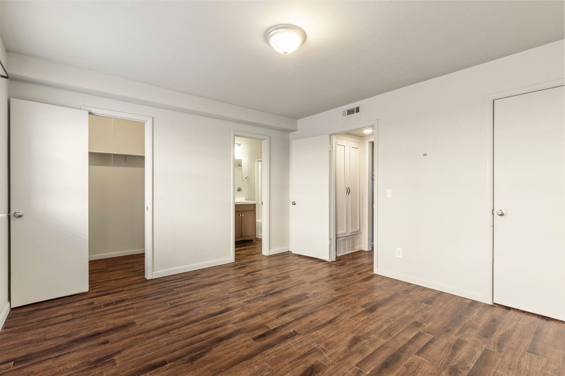 An empty bedroom with hardwood floors and white walls.