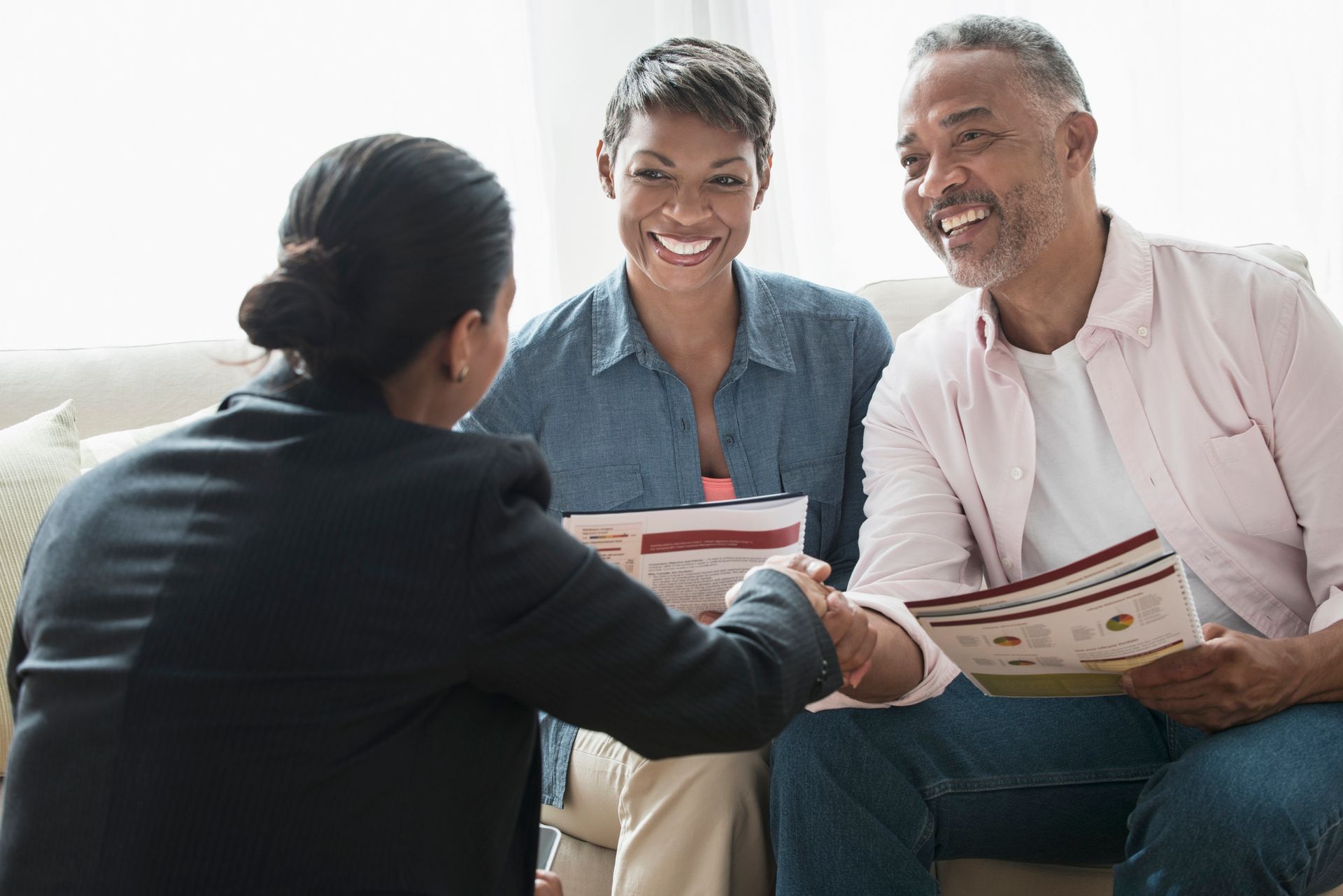 A woman is shaking hands with a man and woman while sitting on a couch.