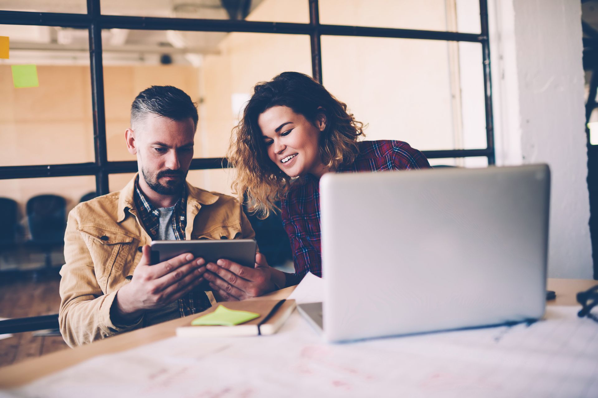 A man and a woman are sitting at a table looking at a tablet.