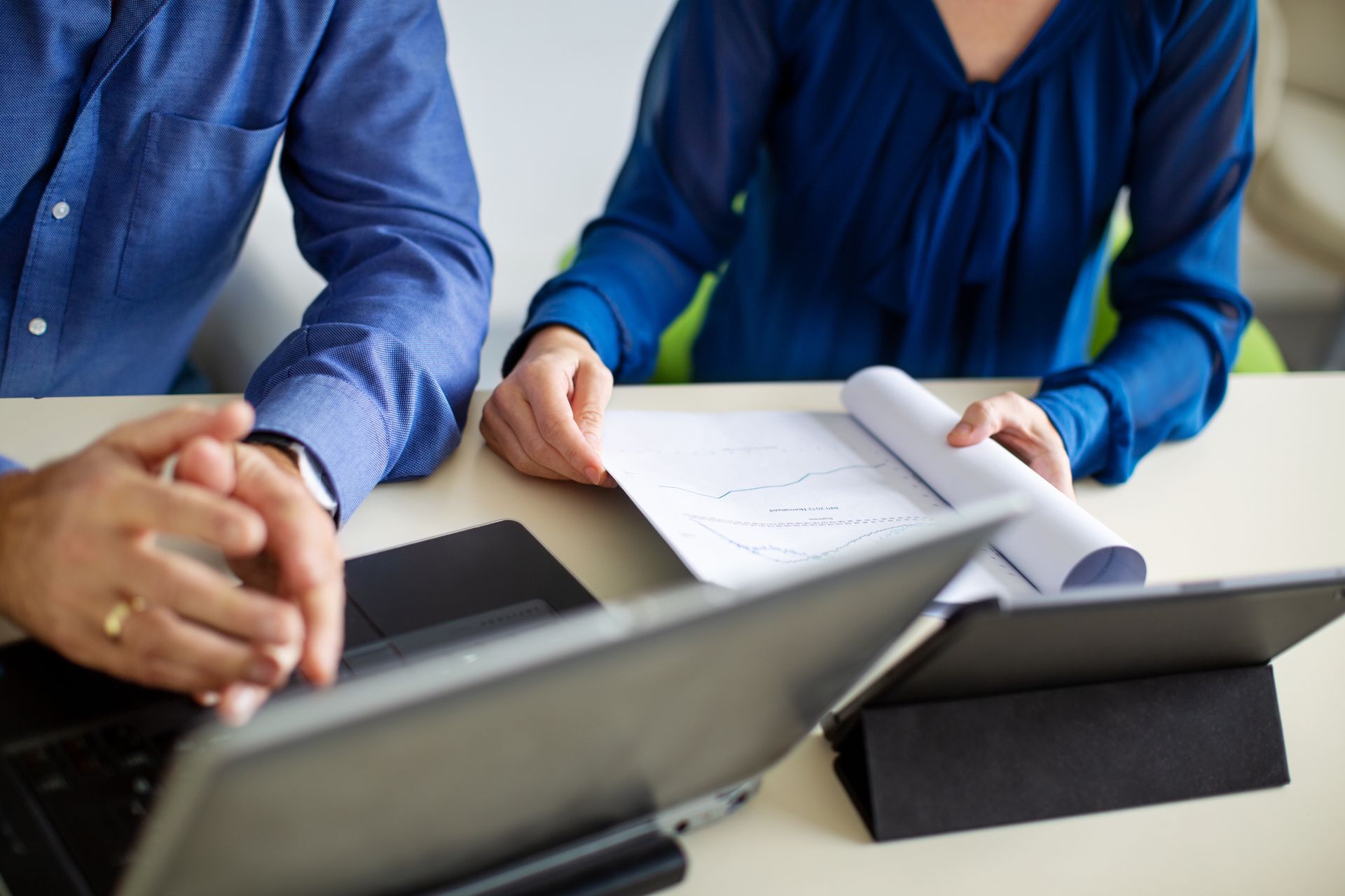 A man and a woman are sitting at a table with laptops and papers.