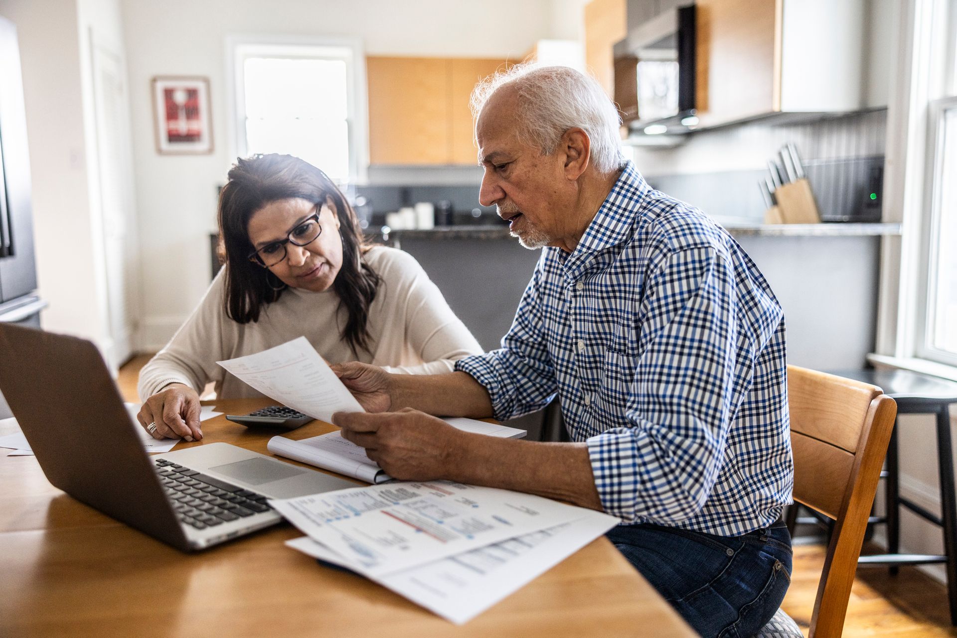 A man and a woman are sitting at a table looking at papers and a laptop.