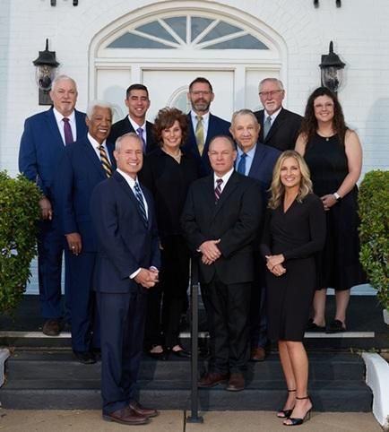 Group of people posing on steps in front of a white building; mostly in suits, smiling.