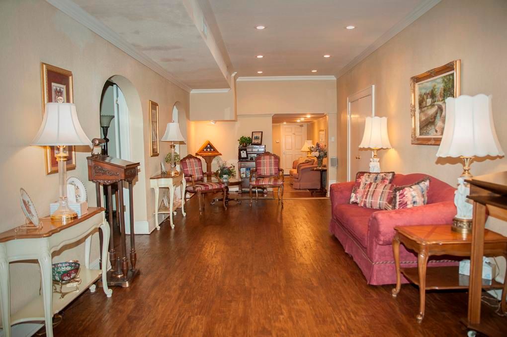 Long hallway with wood flooring, featuring seating areas, lamps, and artwork; neutral tones.