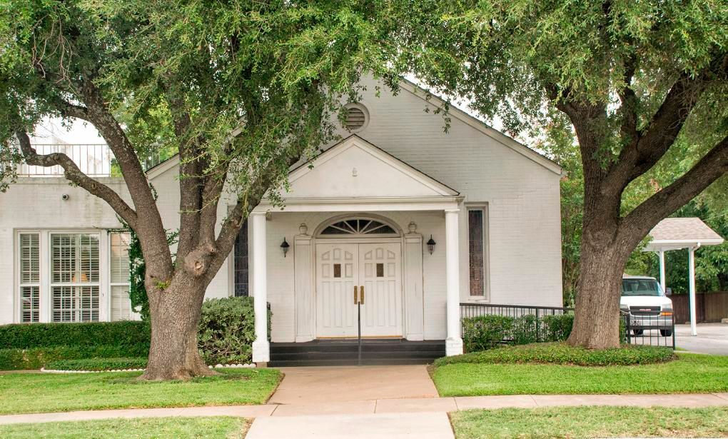 White church building with arched doorway and two large trees framing the front.