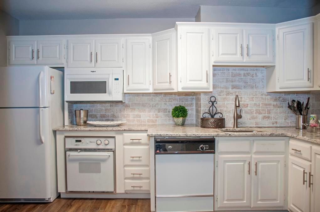 White kitchen with cabinets, appliances, and brick backsplash.