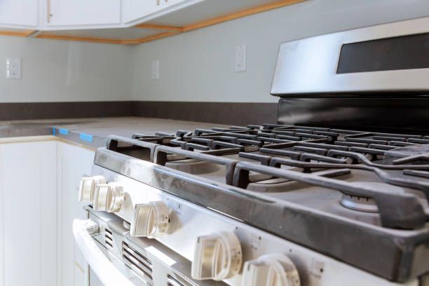 Close-up of a kitchen stove with the burner grates in focus, set against a countertop and wall.