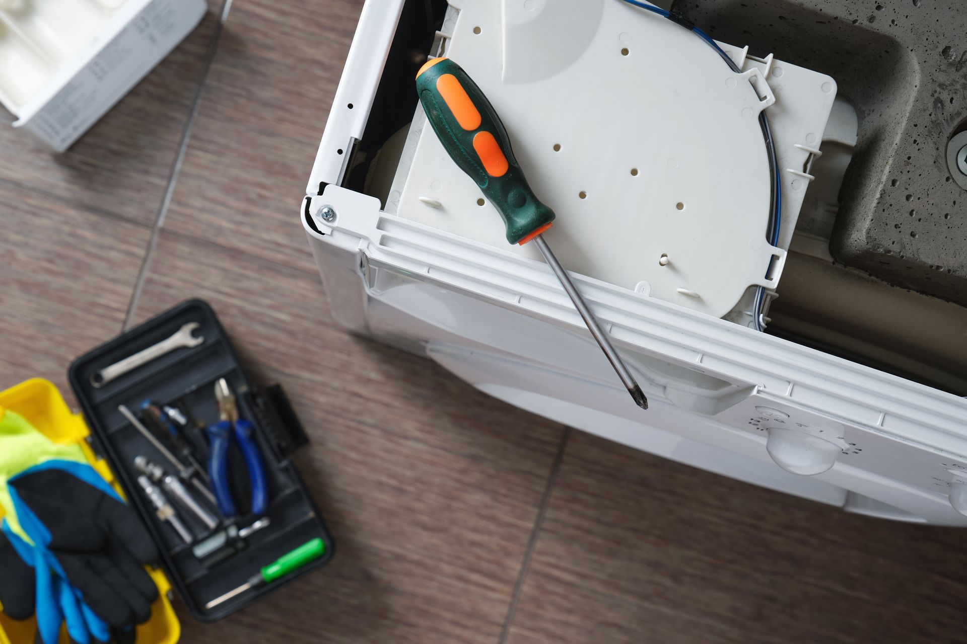 A disassembled appliance being repaired, with tools and a screwdriver, on a tiled floor.