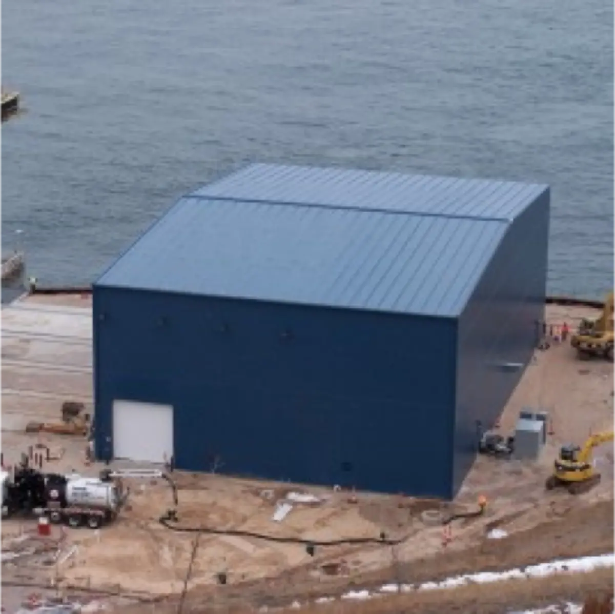 A large blue building with a white door is next to a body of water