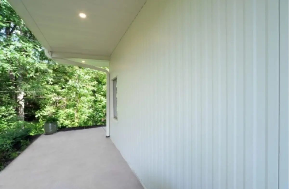 A white house with a porch and trees in the background.
