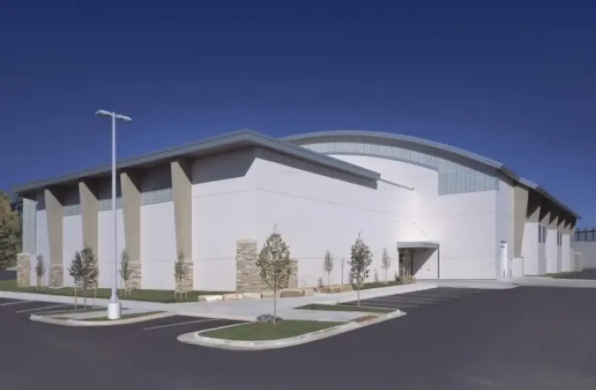 A large white building with a curved roof and a parking lot in front of it