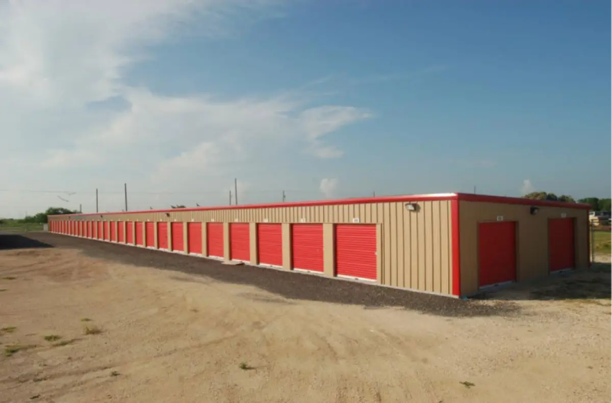 A row of storage units with red doors on a dirt road.