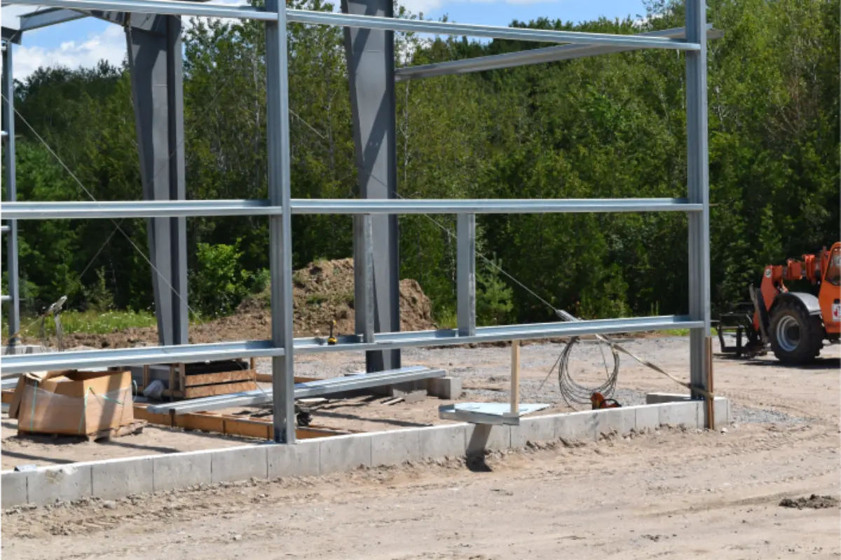 A large metal structure is being built on a dirt road.