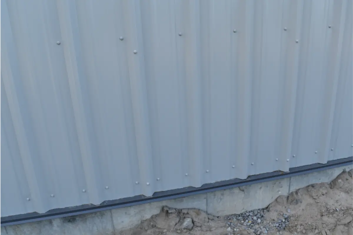 A close up of a gray metal building with a concrete foundation.