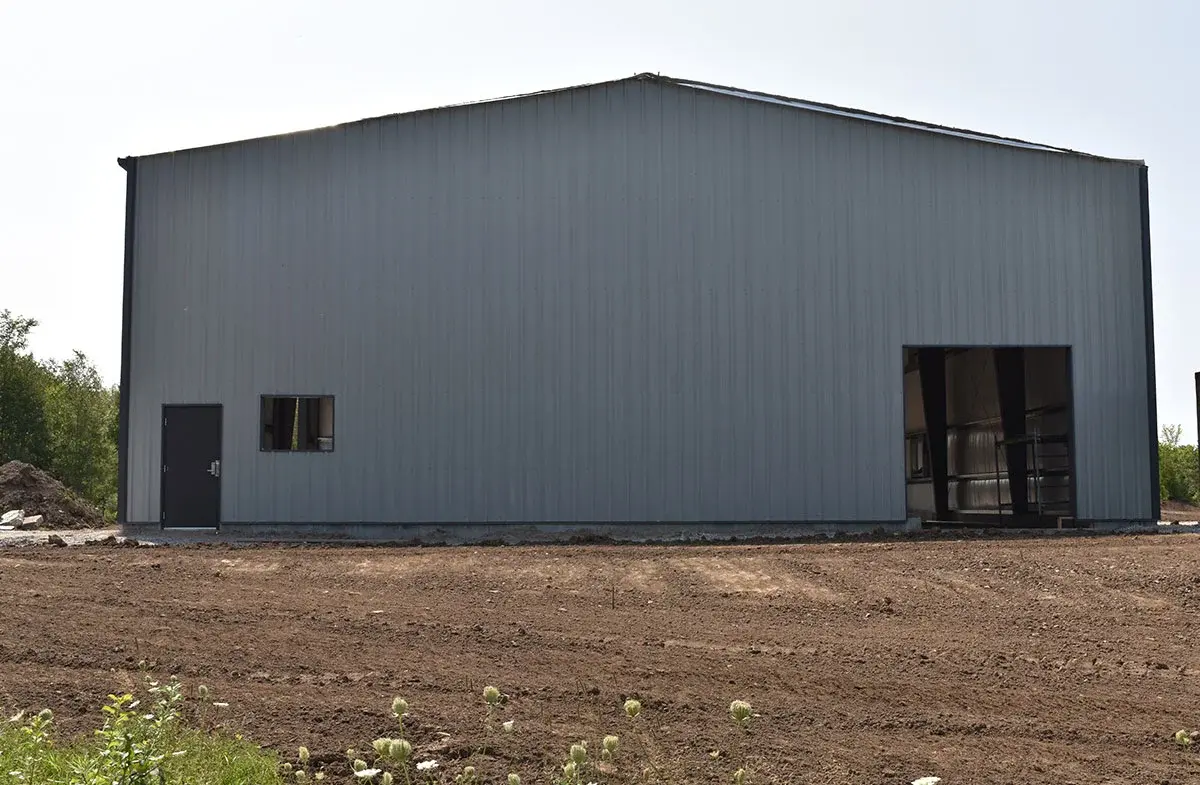 A large metal building is sitting in the middle of a dirt field.