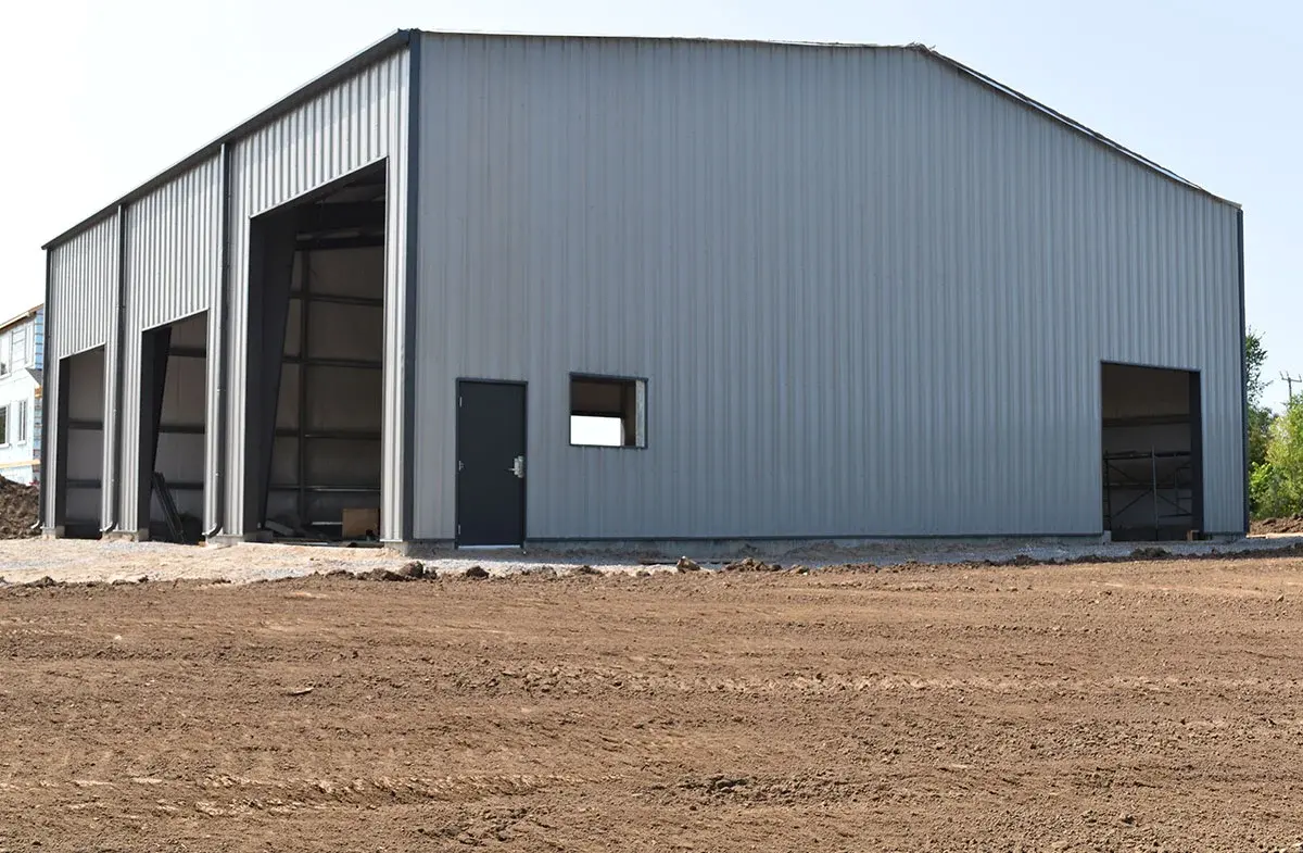 A large metal building is sitting in the middle of a dirt field.