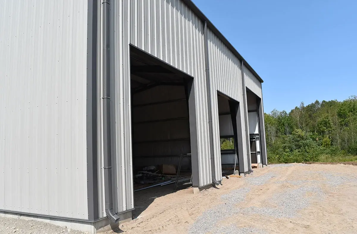 A large metal building with three garage doors is being built.