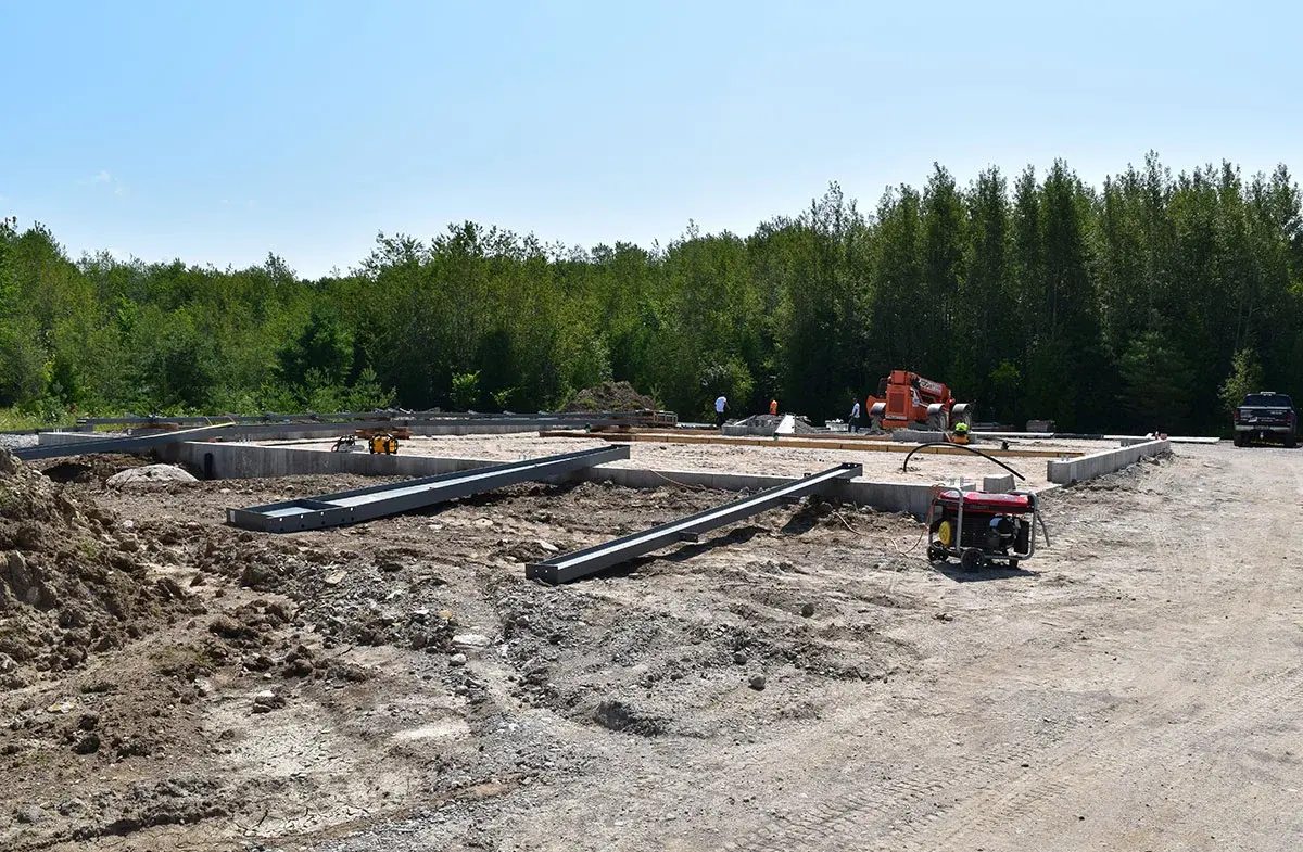 A dirt road leading to a construction site with trees in the background.