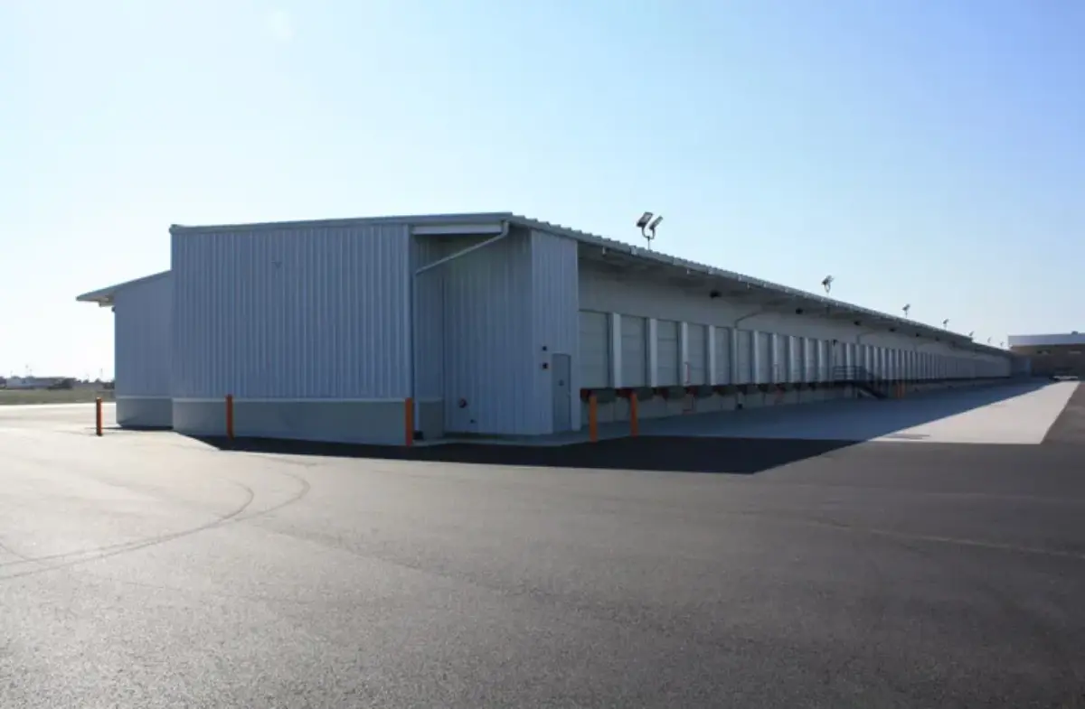 A large white building with a lot of doors is sitting in the middle of a parking lot.