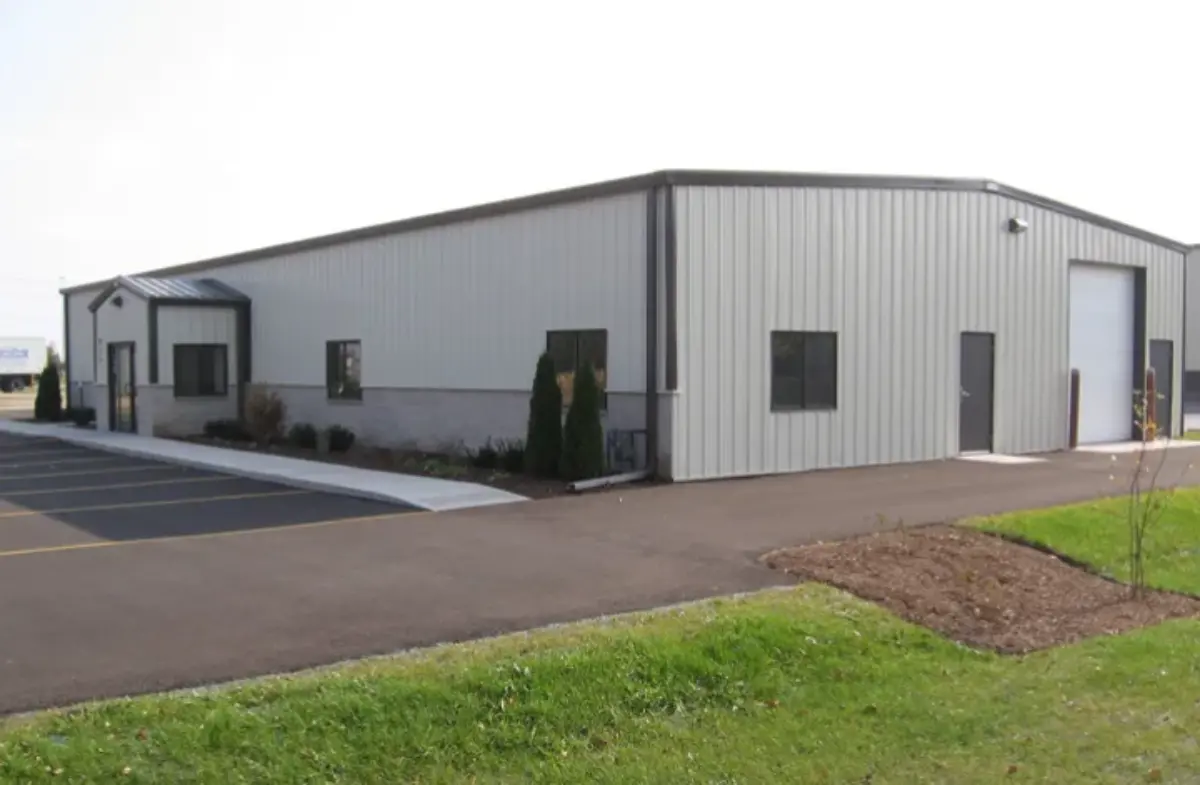A large metal building with a white door is sitting on top of a lush green field.
