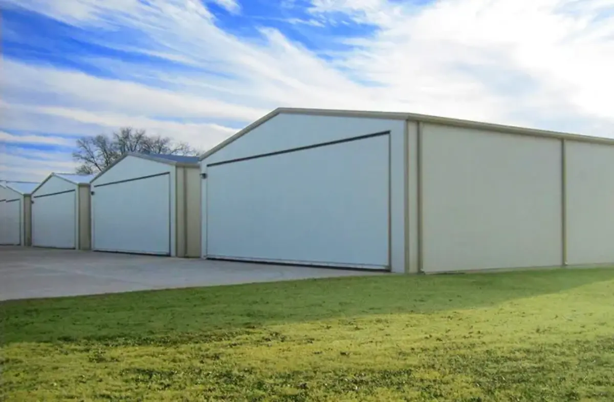 A row of white buildings with sliding doors in a grassy field.