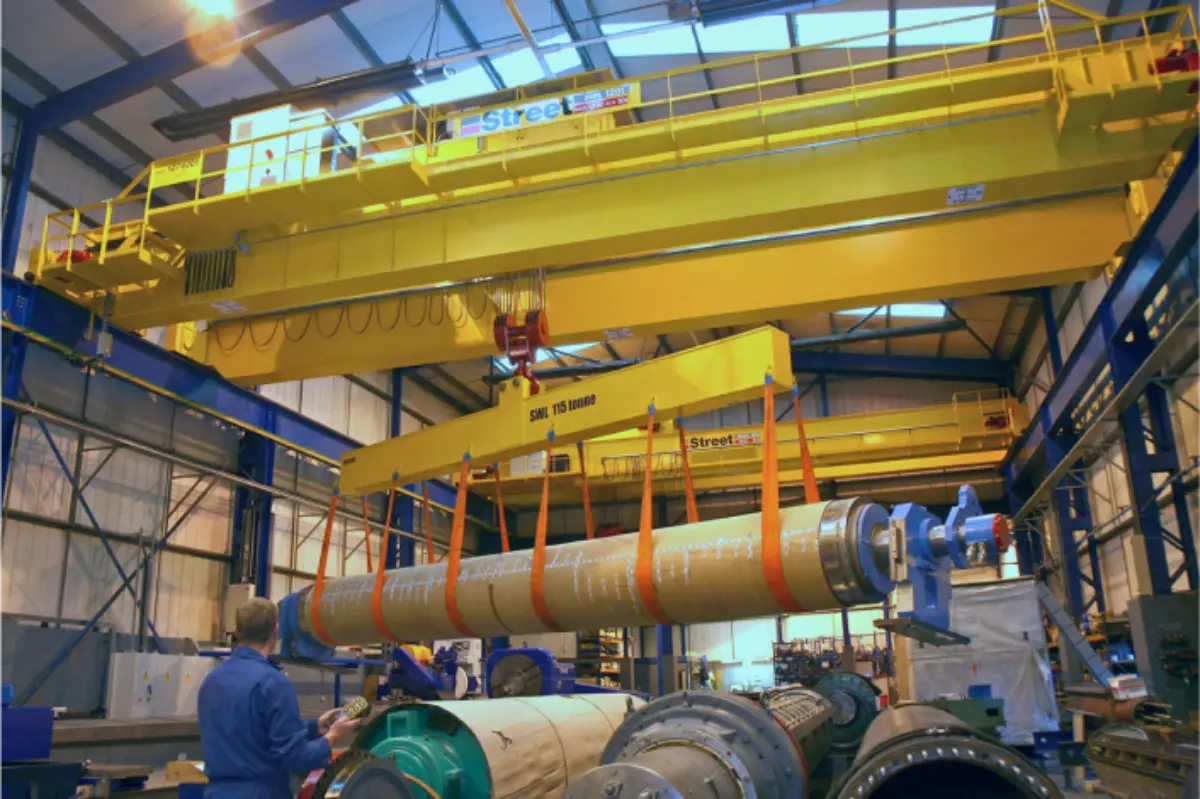 A large pipe is being lifted by a crane in a factory.