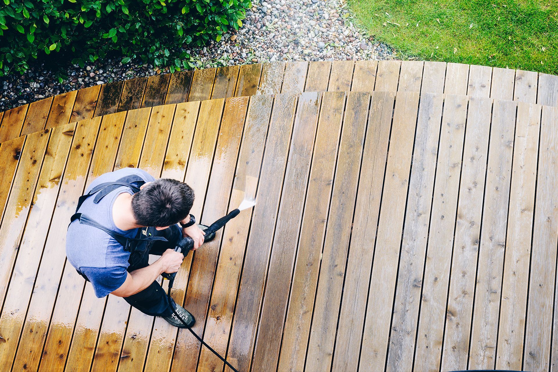 A man is cleaning a wooden deck with a high pressure washer.