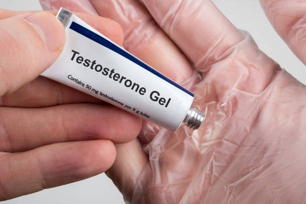Hand holds Testosterone Gel tube with dosage label; gloved hand visible in background