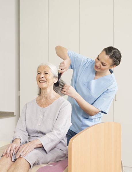 Un'infermiera sta spazzolando i capelli di una donna anziana