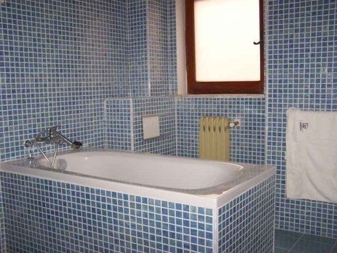 Una vasca da bagno in un bagno con piastrelle blu e una finestra.