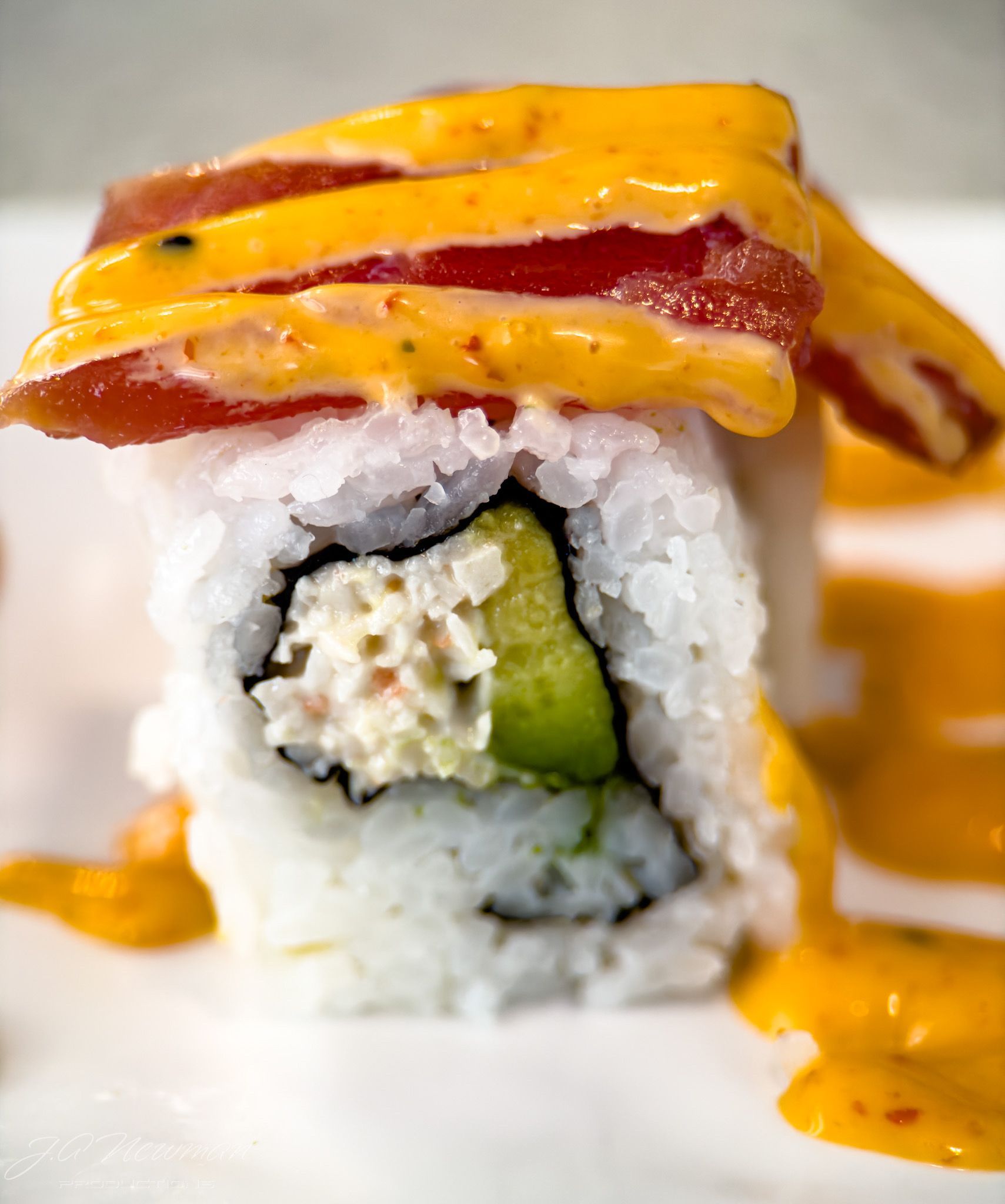 Sushi roll with tuna, avocado, crab, and a yellow sauce.