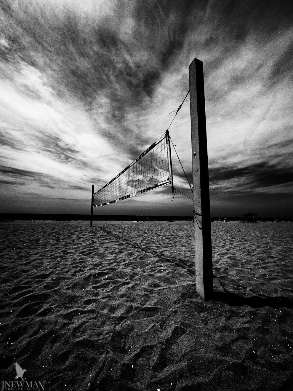 Beach volleyball net on sandy beach under dramatic, cloudy sky.